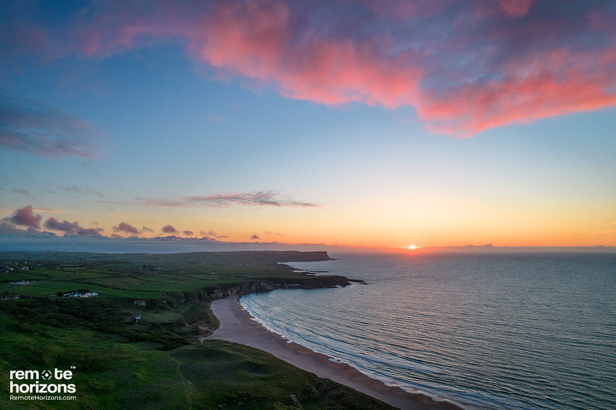 Northern Ireland aerial landscape photography of White Park Bay at sunset with pink clouds.