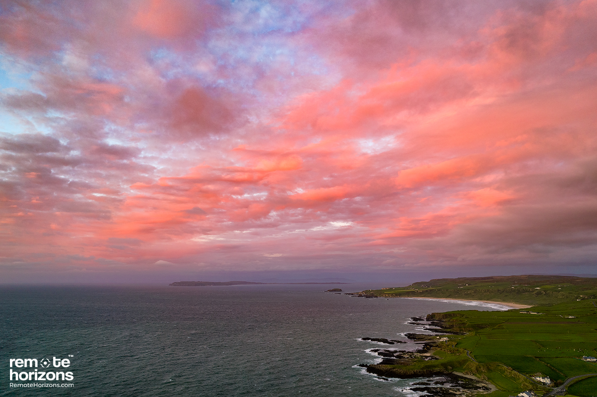 Northern Ireland aerial landscape photography of White Park Bay with a pink sky and Rathlin Island in the distance.